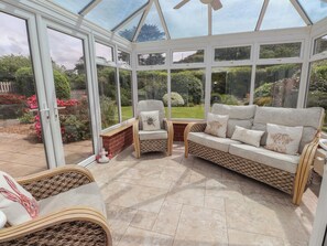 A conservatory with a glass ceiling, wicker furniture, and a garden view. - Bro Mebyd (Criccieth)
