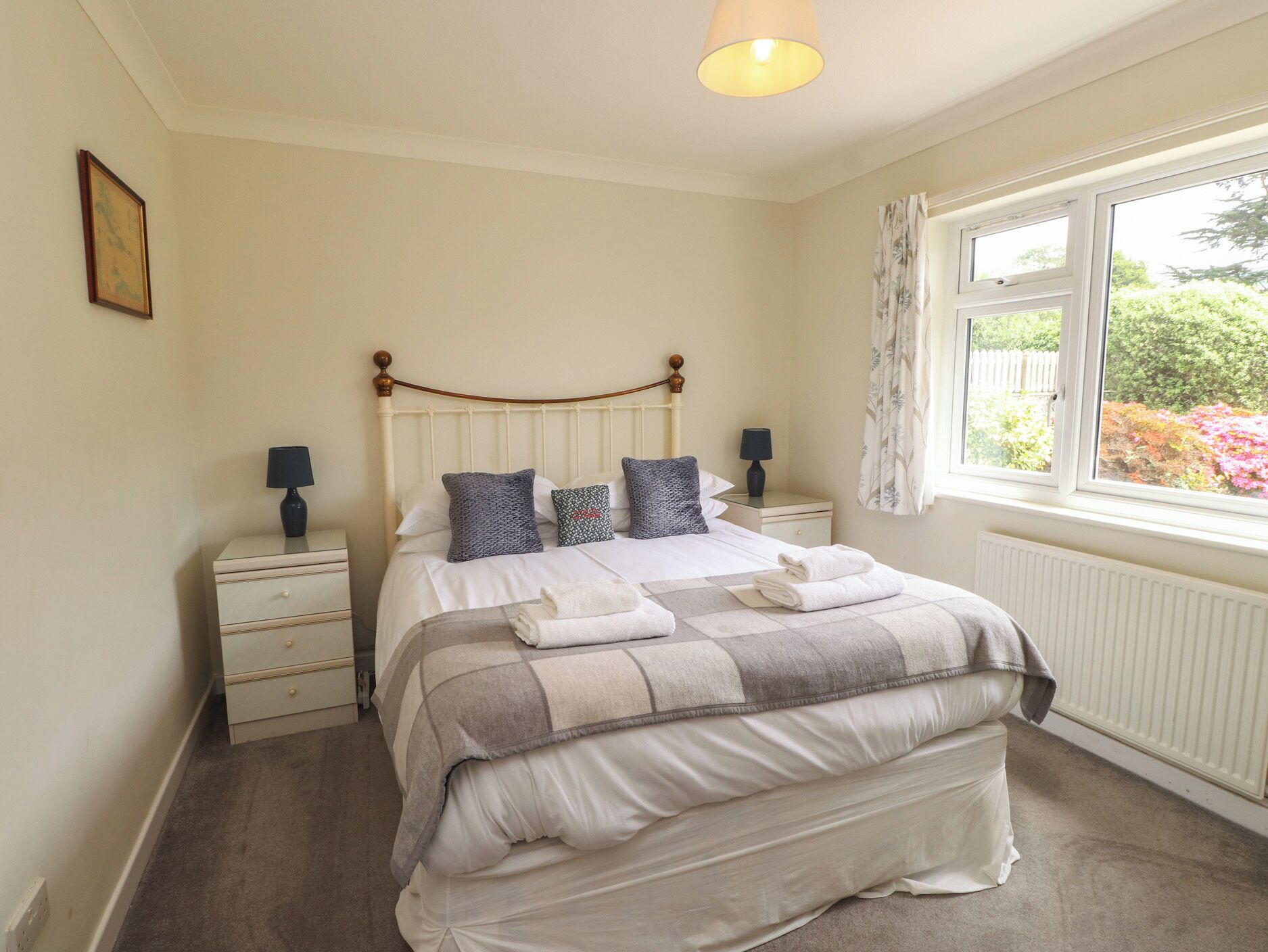 A bedroom with a bed, two bedside tables, a window with curtains, and a radiator.
