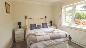 A bedroom with a bed, two bedside tables, a window with curtains, and a radiator.