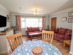 A living room with a sofa, a dining table with chairs, a television, and a chandelier. - Bro Mebyd (Criccieth)
