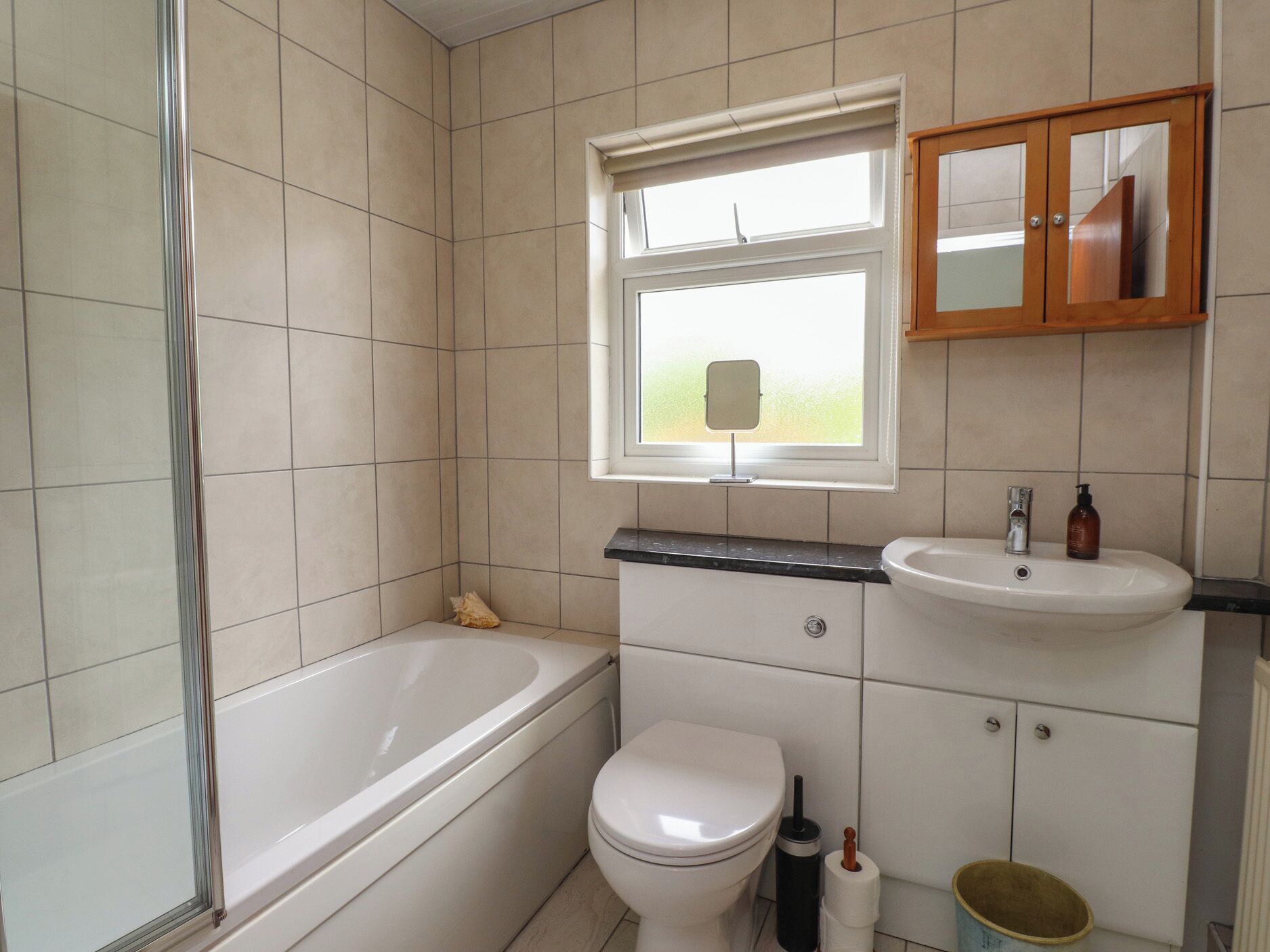 Un baño con bañera, inodoro, lavabo y una ventana con un espejo sobre el lavabo.