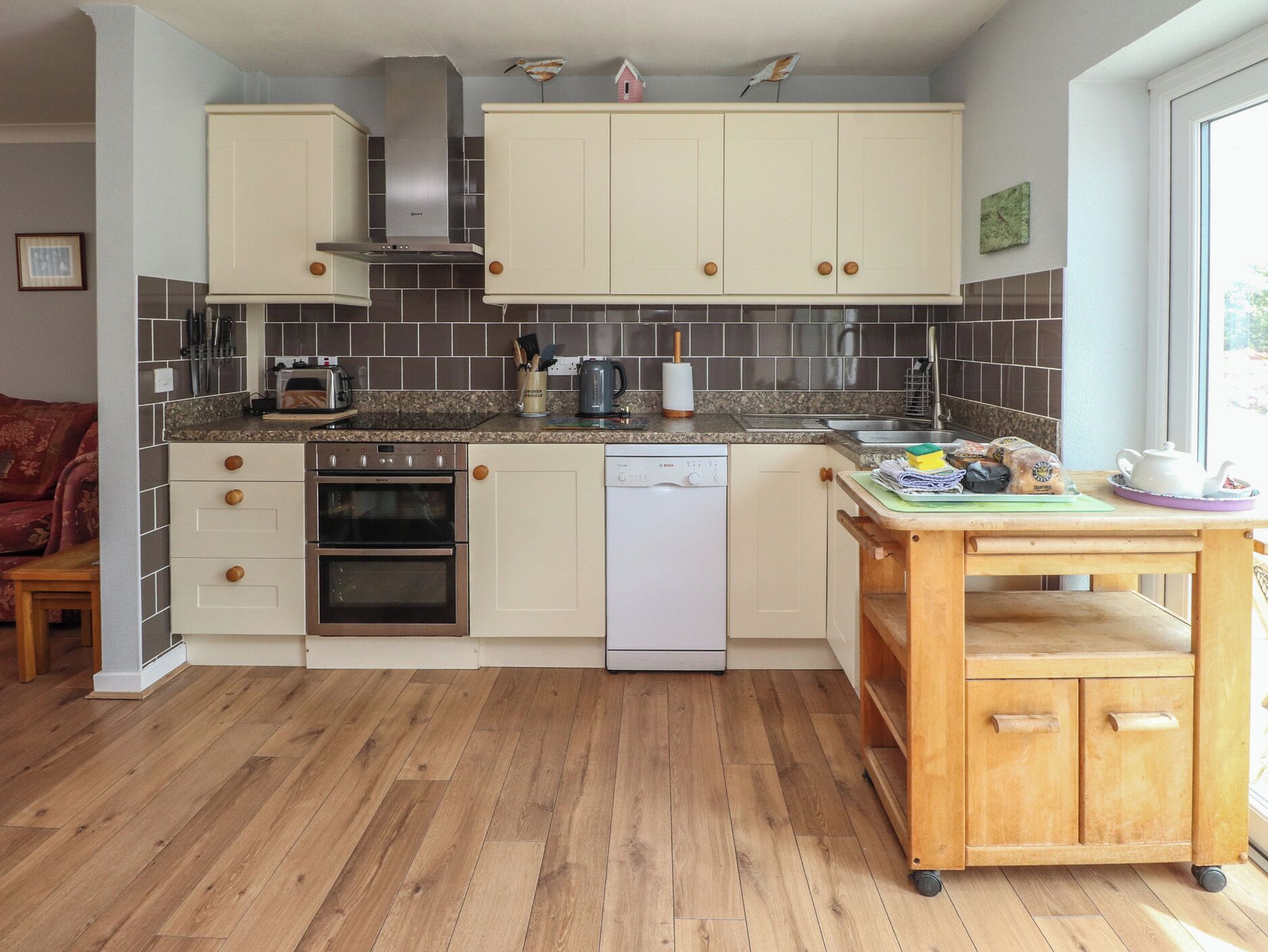 Une cuisine avec des meubles blancs, une hotte de cuisinière en acier inoxydable, un lave-vaisselle et une table en bois avec une planche à découper.