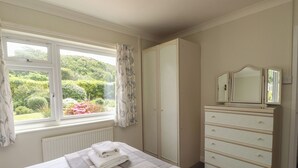 A bedroom with a bed, a dresser, a window with curtains, and a radiator.