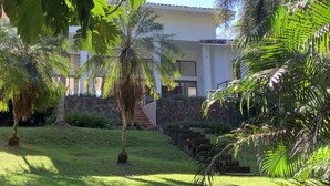 A modern building with a stone staircase leading to a glass door, surrounded by lush greenery and palm trees. - Stunning Oceanfront 4-Bdrm Villa w/ Infinity Pool (Playa Hermosa)