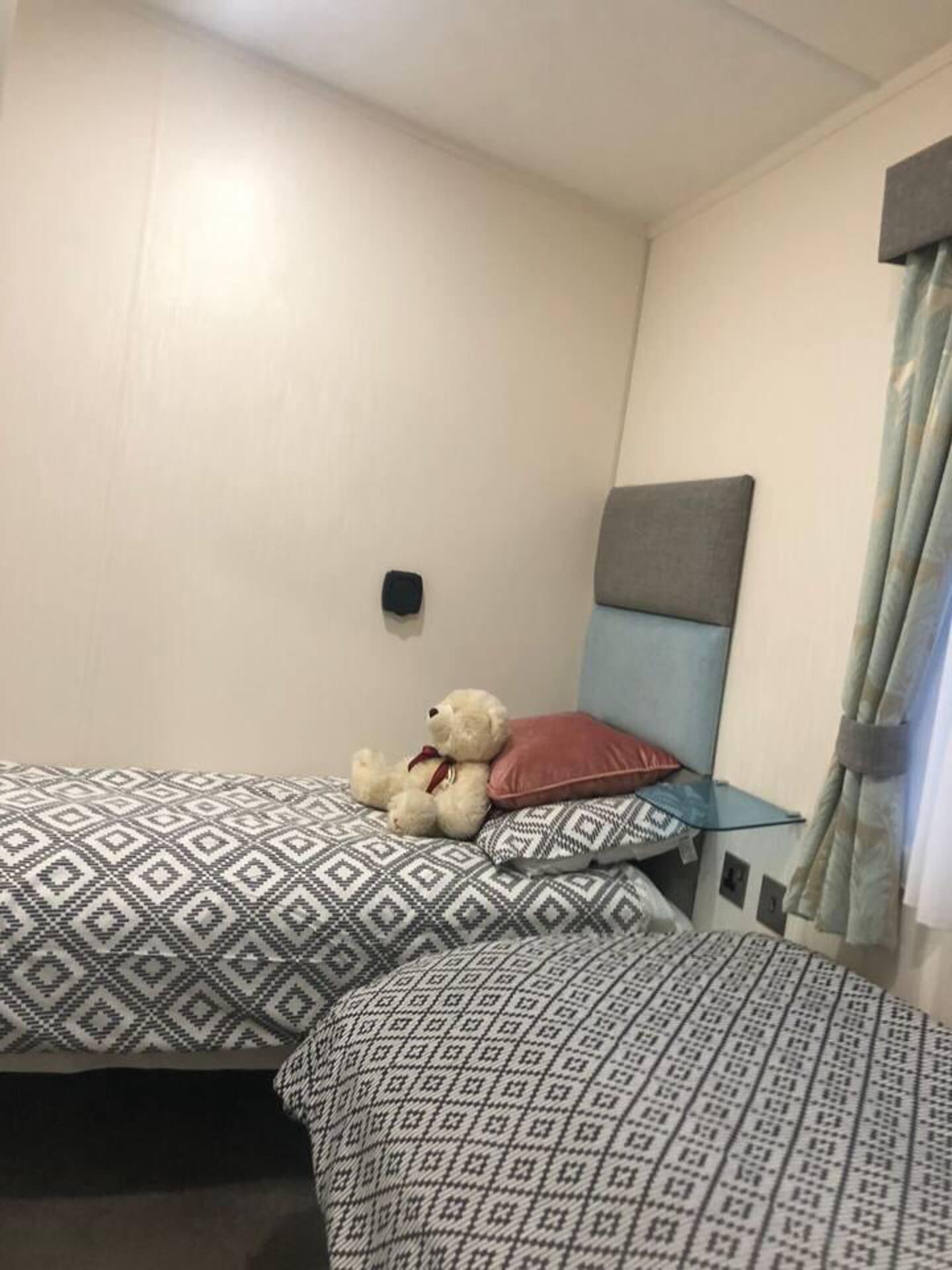 A hotel room with two beds, patterned bedding, a teddy bear, a headboard, and a curtain.