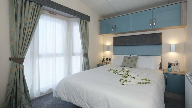 A hotel room with a large bed, two bedside tables, a nightstand, and a wardrobe.