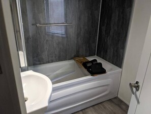A bathroom with a white bathtub, a wooden bench, and a black bag on the bench. - Superior 6 Berth Holiday Home in Suffolk, (Saxmundham)