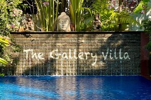 A stone wall with the text "The Gallery Villa" and a pool in front.