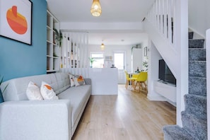 Un salon moderne avec un canapé, un coin repas avec des chaises jaunes et un escalier.
