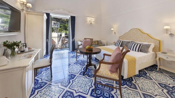Habitación de hotel con cama, escritorio, silla y balcón con vistas a la ciudad.