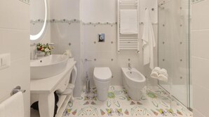 Un baño con lavamanos blanco, inodoro, bidé y cabina de ducha con paredes de vidrio.