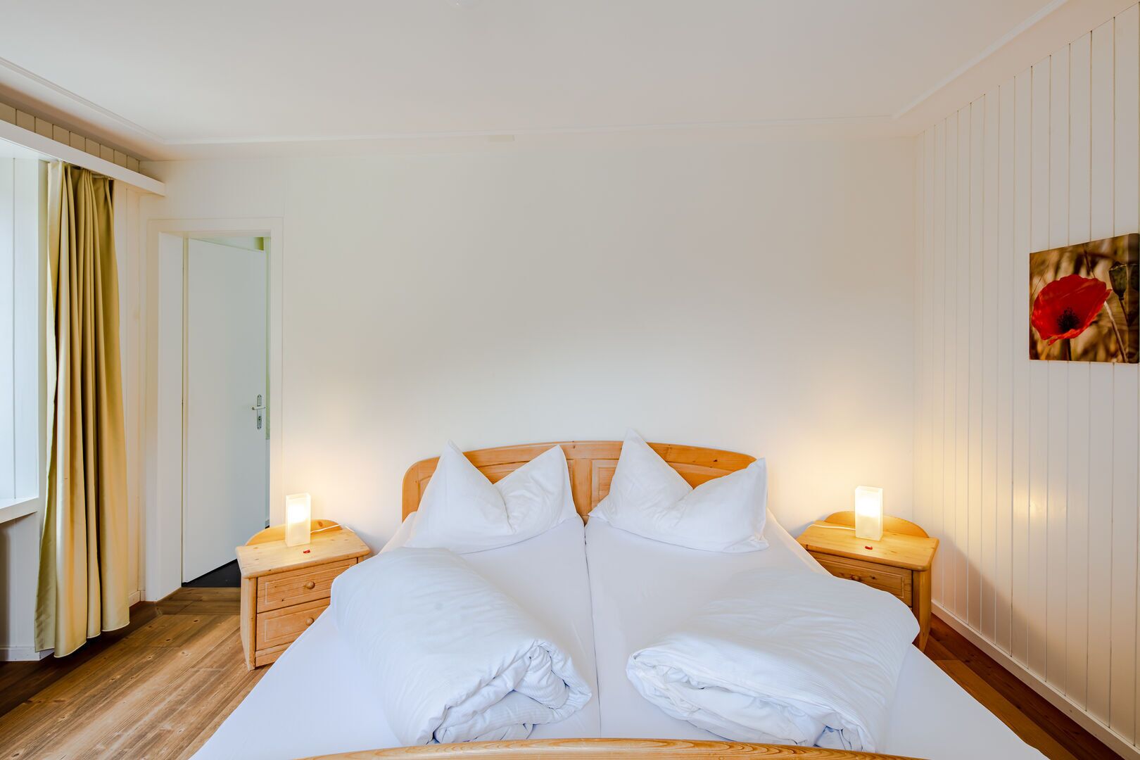Ein Hotelzimmer mit einem großen Bett, einem Holzkopfende, zwei Nachttischen mit Lampen, einer Tür und einer Wand mit einem gerahmten Bild.