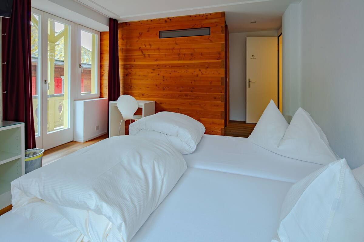 A room with two beds, a desk, a chair, and a wooden wall.