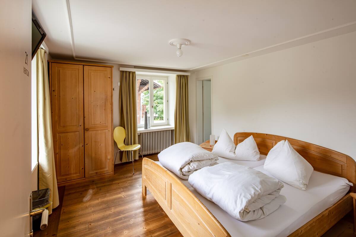 A room with a wooden bed, a chair, a wardrobe, and a window with curtains.
