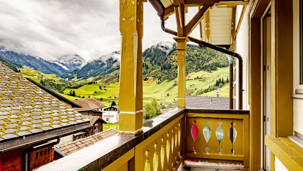 Un balcón amarillo con vistas a un valle verde y montañas.