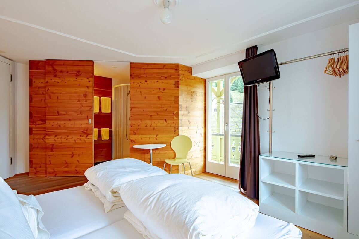 A room with a bed, a small table, a chair, a TV, and a wardrobe.