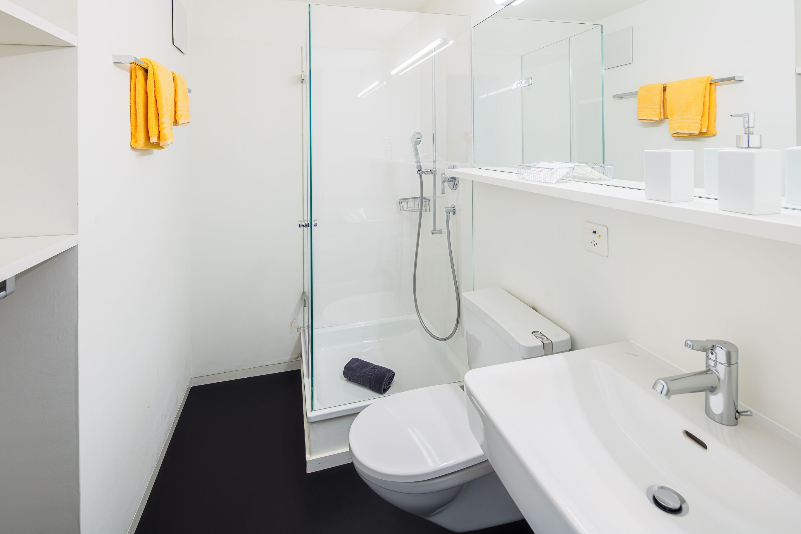 Ein modernes Badezimmer mit Duschkabine aus Glas, einem weißen Waschbecken und einer Toilette.