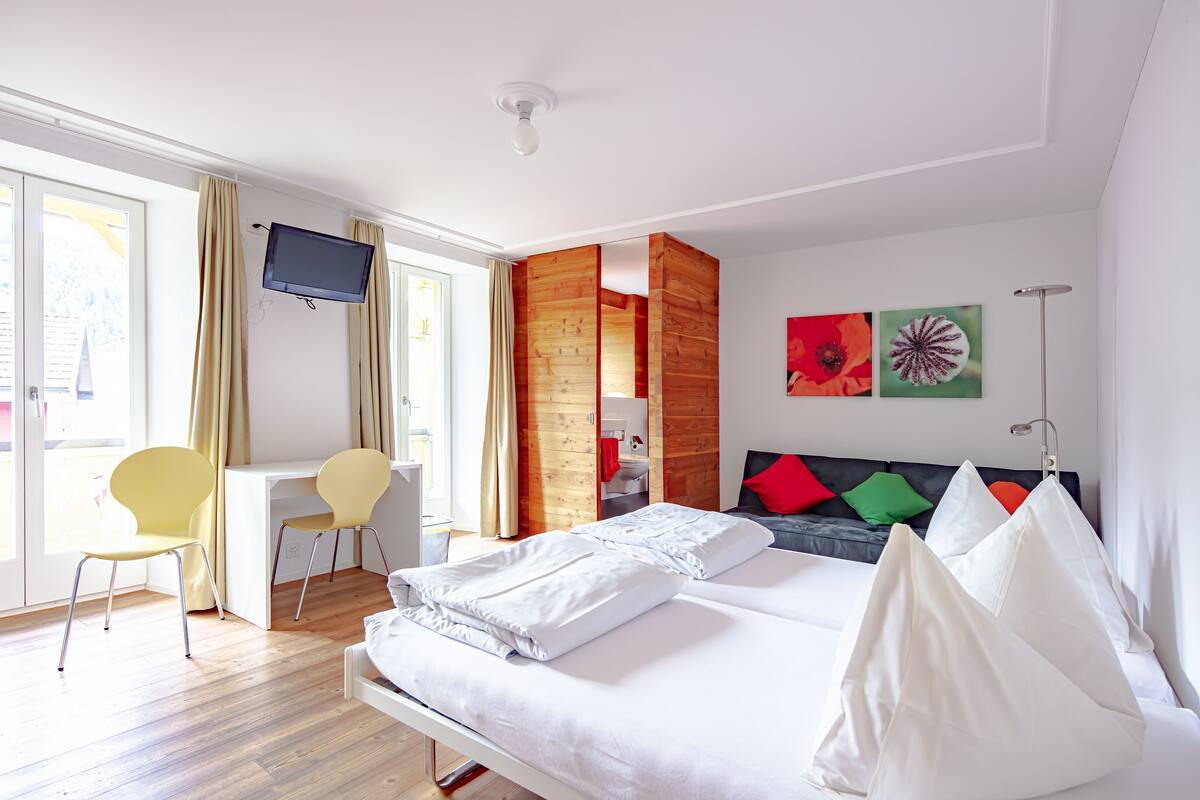 A hotel room with a bed, a desk, a chair, a TV, and a window with curtains.