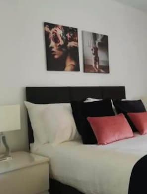 A bedroom with a bed, pillows, a nightstand, and two wall-mounted pictures.