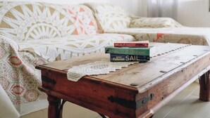 Una mesa de centro de madera con un mantel de encaje, un plaid estampado sobre un sofá, y dos libros titulados 'Final Cut' y 'Sail'.