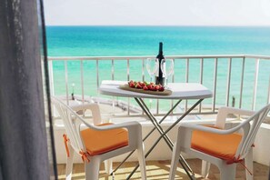 A balcony with a table set for two, overlooking a turquoise sea.
