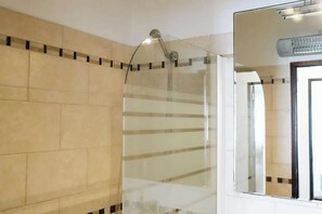 A shower with a glass door, beige tiled walls, and a mirror reflecting the shower area.