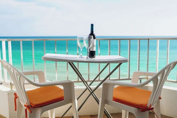 A balcony with a table and two chairs, a bottle of wine, and two glasses.