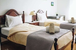 A hotel room with two beds, wooden headboards, white bedding, and a bedside table with a lamp.