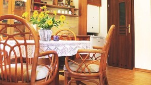 Et spiseområde med et træbord, fletstole og en vase med gule blomster.