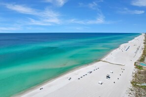 Eine Vogelperspektive eines Strandes mit klarem türkisblauem Wasser, weißem Sand und einer Reihe von Strandsonnenschirmen und Liegestühlen.