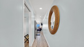 Un couloir doté d’un plancher en bois, d’un grand miroir mural en osier, et donnant sur un salon avec un canapé et un téléviseur.