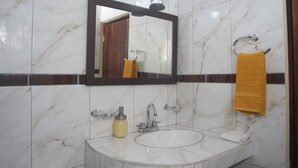 Un baño con lavamanos de mármol, un espejo, un perchero con una toalla amarilla y un dispensador de jabón.