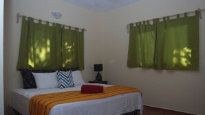 Un dormitorio con cama, cortinas verdes, una mesita de noche y una lámpara.