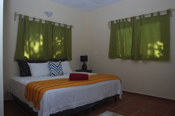 A bedroom with a bed, green curtains, a nightstand, and a lamp.