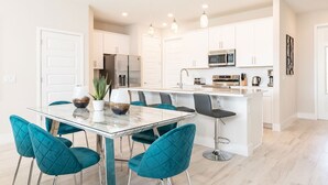 Une cuisine moderne avec des meubles blancs, des appareils en acier inoxydable et un îlot central doté de tabourets de bar.