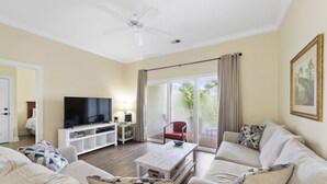 A living room with a flat-screen TV, a white coffee table, beige sofas, a red chair, and a large window with curtains. - BEACH BLISS 2Bedroom/2 Bath condo in Litchfield! (Pawleys Island)