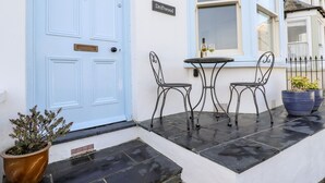A blue door with a nameplate, a small outdoor table with two chairs, and a potted plant. - Driftwood (Fowey)