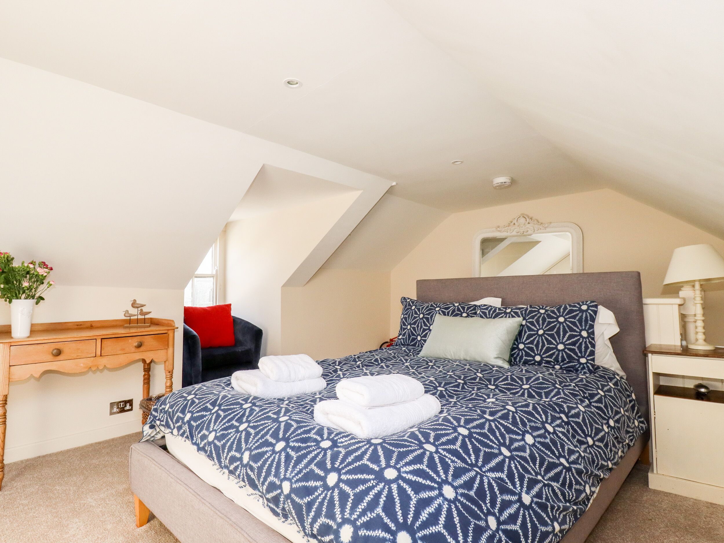 Une chambre à coucher comprenant un lit, une commode, une chaise, un miroir et une lampe.