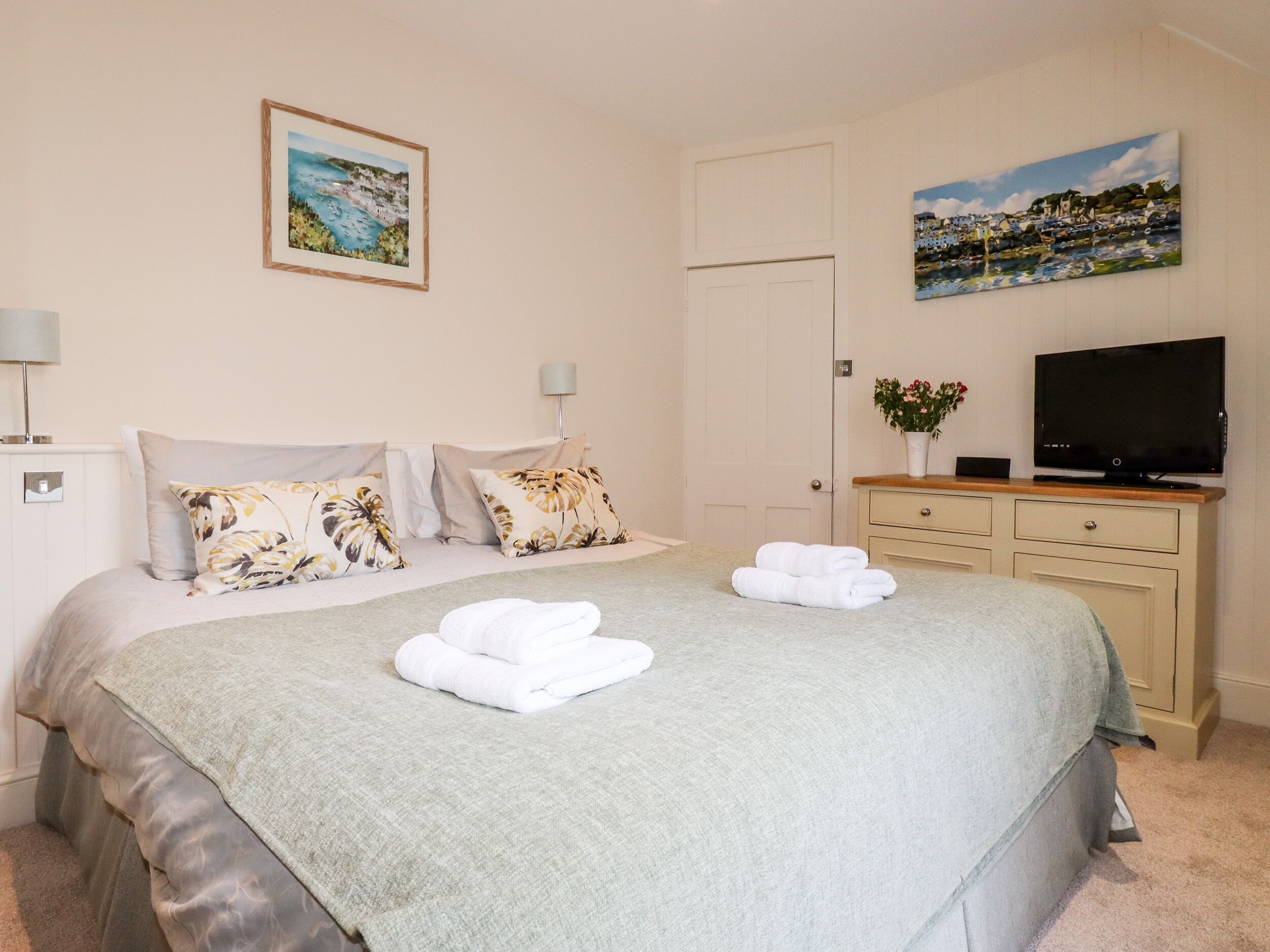 Une chambre à coucher bien rangée, avec un lit, des oreillers, un téléviseur à écran plat, une commode et deux tableaux encadrés accrochés au mur.