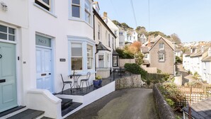 A row of white houses with blue doors, a paved driveway, and a small outdoor seating area with chairs and a table. - Driftwood (Fowey)