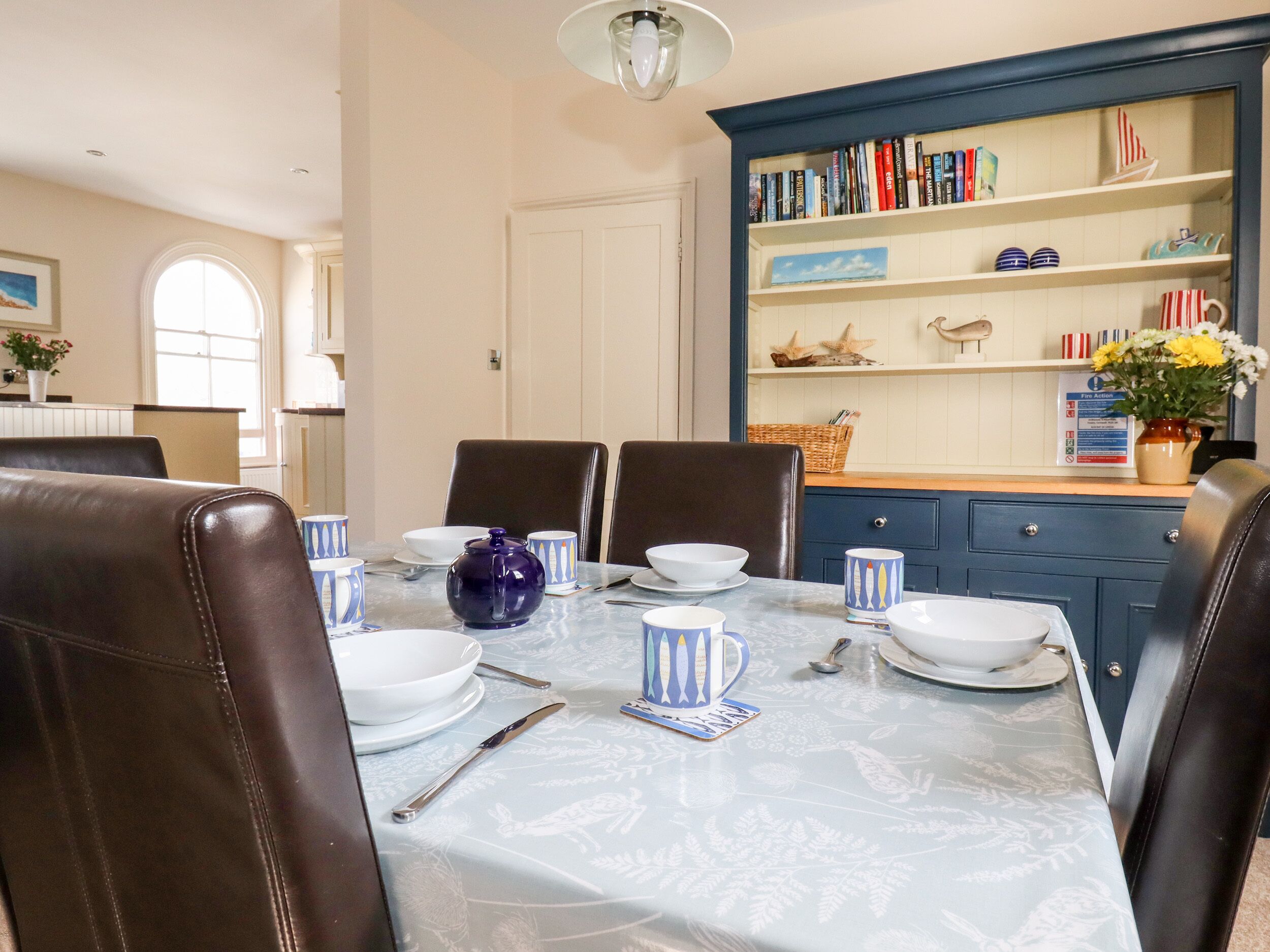 Een eetruimte met een tafel voor vier personen, omringd door lederen stoelen. Achtergrond toont een boekenkast met boeken en decoratieve objecten.