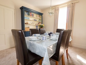 A dining room with a table set for six, surrounded by leather chairs. A blue bookshelf with various items is against the wall.