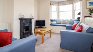 A living room with a fireplace, a television, a sofa, and a window seat. - Driftwood (Fowey)