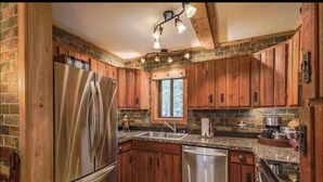 Una cocina con armarios de madera, un refrigerador de acero inoxidable, lavavajillas y encimera de granito.