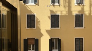 Eine Gebäudefassade mit mehreren Fenstern, von denen einige Fensterläden haben, und einem Metallgeländer im Vordergrund.