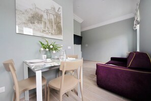 A dining area with a table, chairs, a vase with flowers, and a purple sofa. - Colosseo Gardens - C13 (Rome)