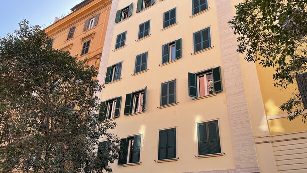 Ein mehrgeschossiges Gebäude mit einer beige farbenen Fassade, grünen Fensterläden und einem Schild mit der Aufschrift 'Colosseo Gardens'.