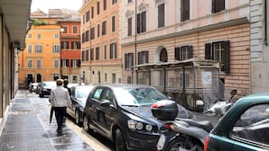 Una calle estrecha bordeada por coches aparcados y edificios de arquitectura clásica.