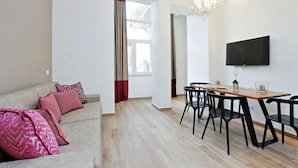 Una sala de estar moderna con un sofá, una mesa de comedor con sillas, un televisor montado en la pared y una araña.