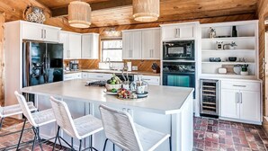 Une cuisine moderne avec des meubles blancs, un grand îlot central doté de tabourets et un sol en briques.